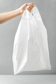 consumerism and eco friendly concept - woman holding white disposable plastic bag over grey background