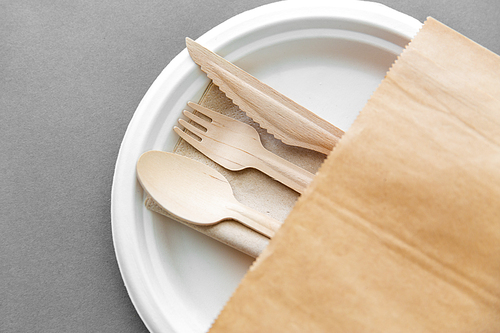 cutlery, recycling and eco friendly concept - set of wooden spoon, fork and knife on paper plate on grey background