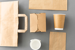 package, recycling and eating concept - disposable paper container for takeaway food, coffee cups and bags on grey background
