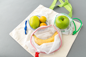 food shopping, reuse and ecology concept - reusable bags with fruits on grey background