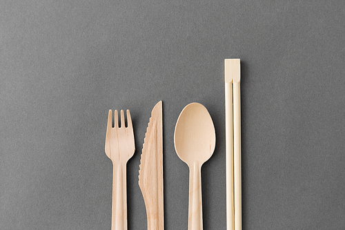 cutlery, recycling and eco friendly concept - wooden disposable spoon, fork, knife and chopsticks on grey background