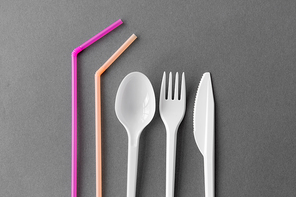 eating, recycling and ecology concept - white disposable plastic fork, knife and spoon with pink straws on grey background