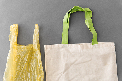 consumerism, recycling and eco friendly concept - reusable canvas tote for food shopping and plastic bag on grey background
