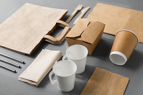 package, recycling and eating concept - disposable paper container for takeaway food with cups, bags, napkins and cutlery on table