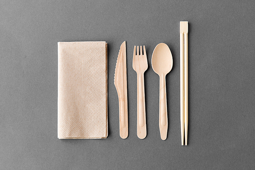 cutlery, recycling and eco friendly concept - wooden disposable spoon, fork, knife with chopsticks and paper napkin on grey background