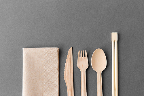 cutlery, recycling and eco friendly concept - wooden disposable spoon, fork, knife with chopsticks and paper napkin on grey background