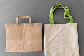 consumerism, recycling and eco friendly concept - reusable canvas tote for food shopping and paper bag on grey background