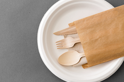 cutlery, recycling and eco friendly concept - set of wooden spoon, fork and knife on paper plate on grey background