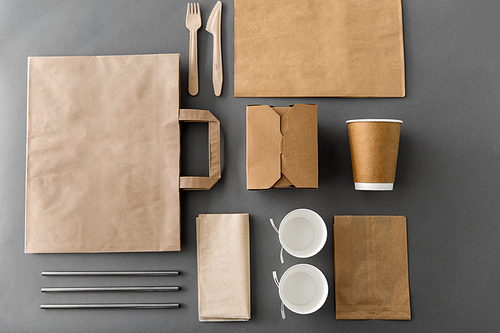 package, recycling and eating concept - disposable paper container for takeaway food with cups, bags, napkins and cutlery on table