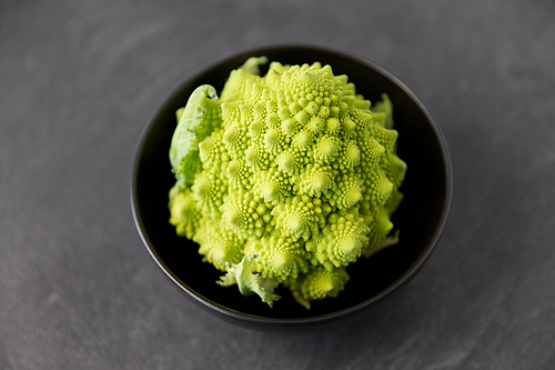 vegetable, food and culinary concept - close up of romanesco broccoli in ceramic bowl on slate stone background