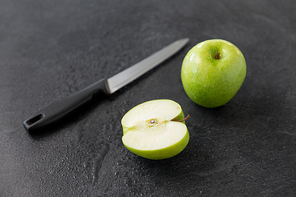 fruits, diet, eco food and objects concept - green apples and kitchen knife on slate stone background