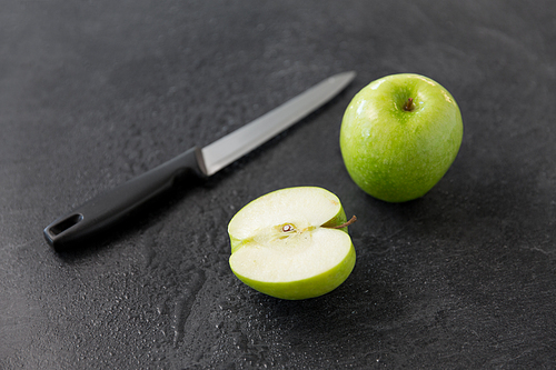 fruits, ,  food and objects concept - green apples and kitchen knife on slate stone background