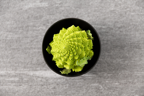 vegetable, food and culinary concept - close up of romanesco broccoli in ceramic bowl on slate stone background