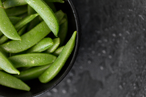 vegetable, food and culinary concept - close up of peas in bowl on wet slate stone background