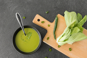 vegetable, food and culinary concept - bok choy chinese cabbage cream soup in ceramic bowl with spoon on slate stone background