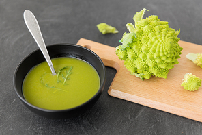 vegetable, food and culinary concept - close up of romanesco broccoli cream soup in ceramic bowl on slate stone background