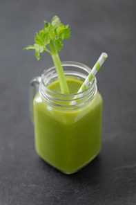 healthy eating, detox and vegetable diet concept - close up of glass mug of green fresh celery juice or smoothie with paper straw on slate stone background