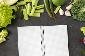 food, diet and healthy eating concept - close up of different green vegetables and diary with empty pages on slate stone background