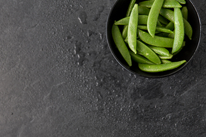 vegetable, food and culinary concept - peas in bowl on wet slate stone background