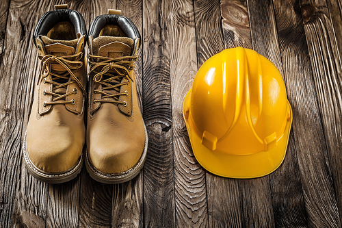 construction safety tools yellow helmet and leather working boots on vintage wooden background