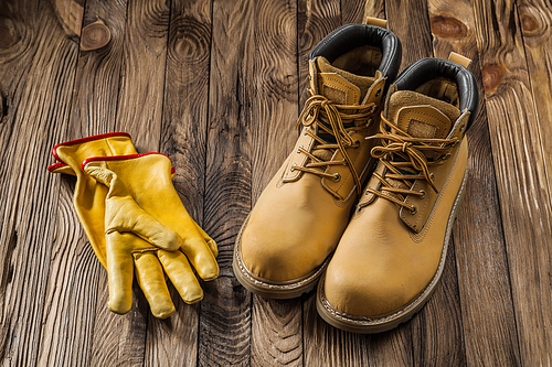 construction safety tools yellow working gloves and leather working boots on vintage wooden background