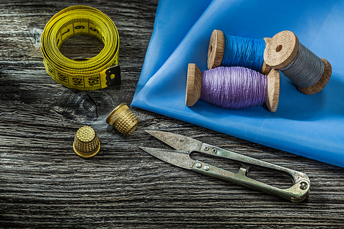 sewing tools spools with threads scissors thimbles measure tape on vintage wooden background