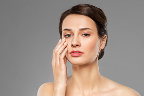 beauty, bodycare and people concept - beautiful young woman touching her face over grey background