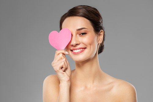 valentines day, beauty and love concept - happy smiling young woman closing one eye with pink heart shape over grey background