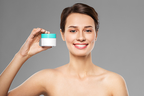 beauty, cosmetics and skincare concept - happy young woman holding jar of cream over grey background