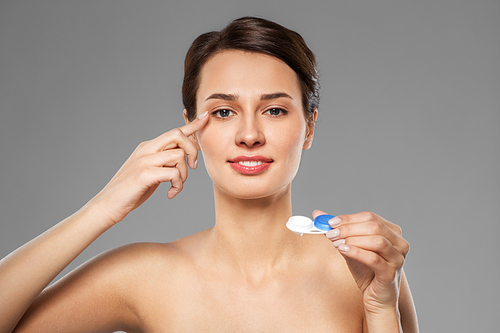 health, vision and old people concept - happy smiling young woman putting on contact lenses over grey background