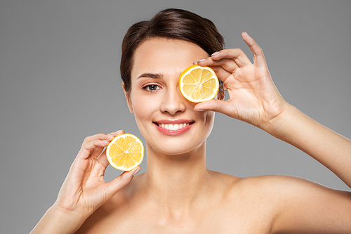 beauty, skin care and detox concept - beautiful woman making eye mask of lemon slices over grey background