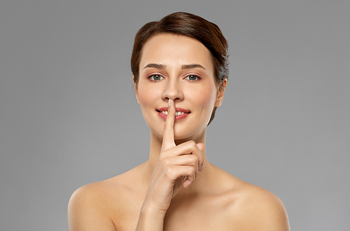 beauty secret, silence and people concept - beautiful young woman holding finger on lips over grey background