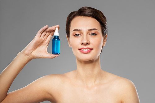 beauty, cosmetics and skincare concept - happy young woman with bottle of serum over grey background