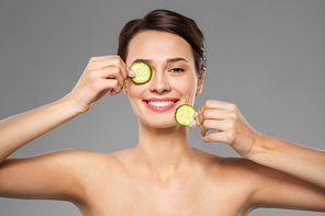 beauty, skin care and detox concept - beautiful woman making eye mask of cucumbers over grey background