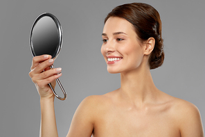 beauty, bodycare and people concept - beautiful young woman with bare shoulders looking to mirror over grey background