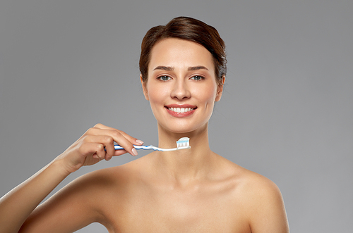 oral hygiene, dental care and health concept - smiling woman with toothpaste on toothbrush cleaning teeth over grey background