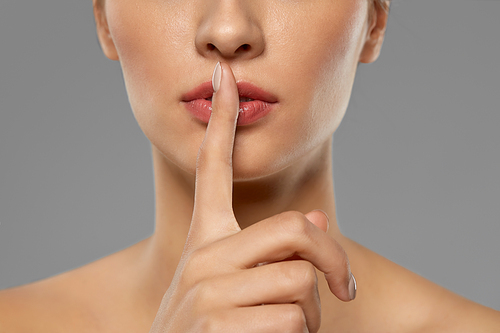 beauty secret, silence and people concept - close up of beautiful young woman holding finger on lips over grey background