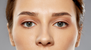 beauty, makeup and vision concept - close up of beautiful young woman face and eyes over grey background