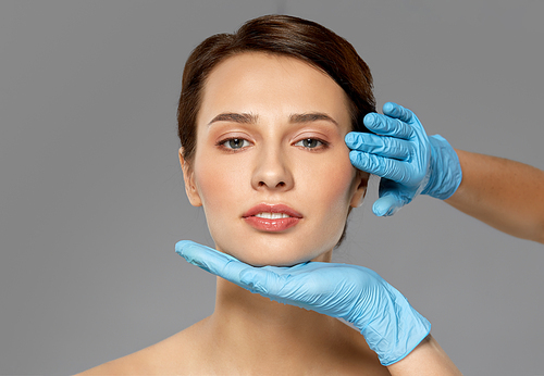 cosmetology, plastic surgery and beauty concept - beautiful young woman face and hands in surgical gloves over grey background and snow
