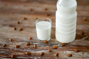 food and dairy products concept - glass and bottle of milk and almond nuts on wooden table
