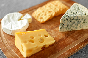food and eating concept - different kinds of cheese and salty crackers on wooden cutting board