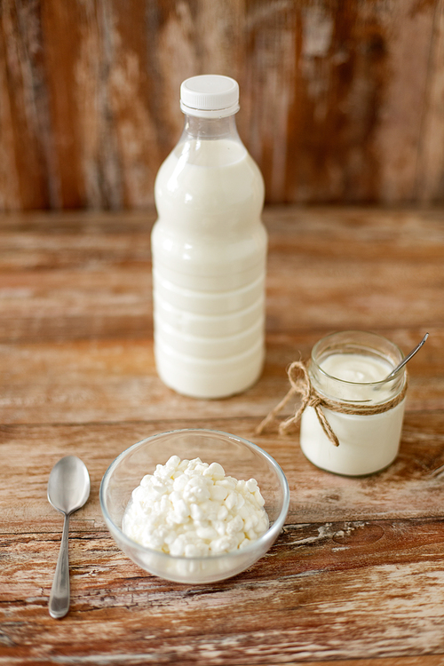 food and dairy products concept - bottle of milk, cottage cheese and homemade yogurt on wooden table