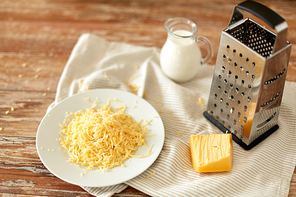 food, cooking and eating concept - close up of grated cheese, grater and jug of milk on wooden table