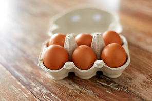 food, culinary and cooking concept - close up of natural chicken eggs in cardboard box on wooden table