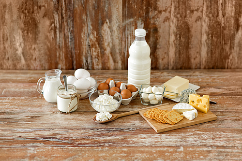 food and eating concept - close up of cottage cheese, crackers, bottle of milk, yogurt with butter and chicken eggs on wooden table