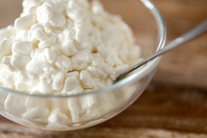 food and dairy products concept - close up of homemade cottage cheese in glass bowl on wooden table