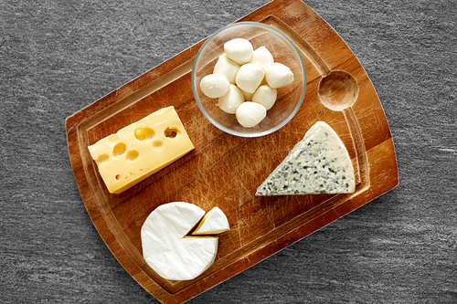 food and eating concept - different kinds of cheese on wooden cutting board