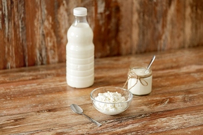 food and dairy products concept - bottle of milk, cottage cheese and homemade yogurt on wooden table