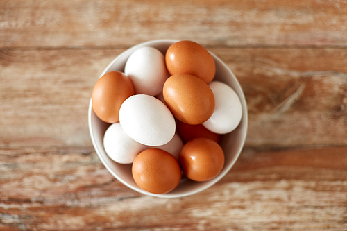 food, culinary and cooking concept - close up of natural chicken eggs in ceramic bowl on wooden table