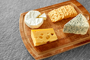 food and eating concept - different kinds of cheese and salty crackers on wooden cutting board